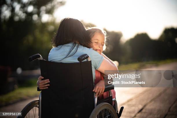 kind mit geschlossenen augen umarmt ihre mutter im rollstuhl - child in wheelchair stock-fotos und bilder