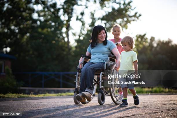 moeder in rolstoel whit haar kinderen die tijd in openlucht doorbrengen - assistant family stockfoto's en -beelden
