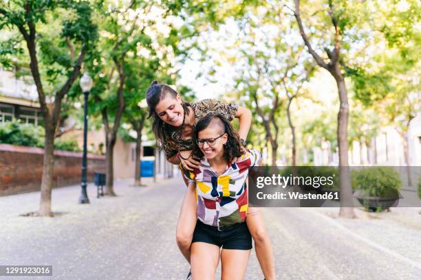 lesbian couple doing piggyback while standing on footpath in city - lesbian date stock-fotos und bilder