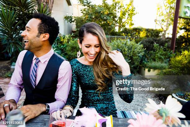 cheerful woman and man enjoying while sitting at dining table in back yard during party - woman in cocktail dress stock pictures, royalty-free photos & images