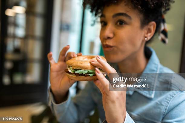 mid adult woman eating burger while sitting at cafe - veggie burger stock pictures, royalty-free photos & images