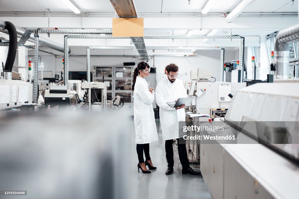 Male and female scientists discussing over laptop by machinery at laboratory