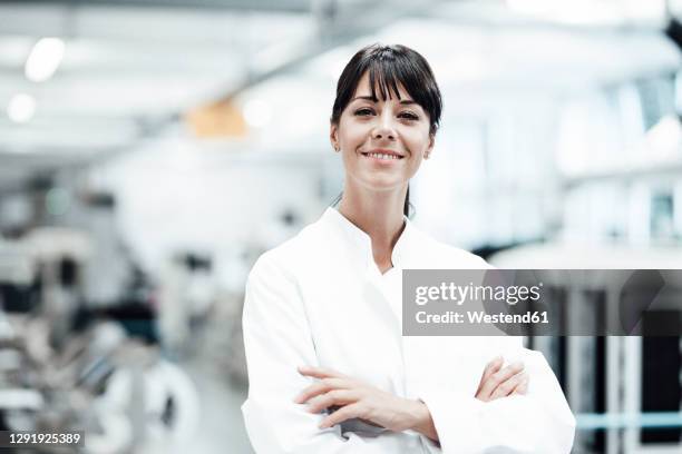 smiling female scientist standing with arms crossed in bright laboratory - female scientist ストックフォトと画像
