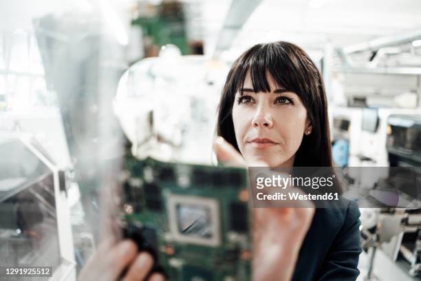 confident female professional investigating while looking at circuit board in industry - chips stock-fotos und bilder