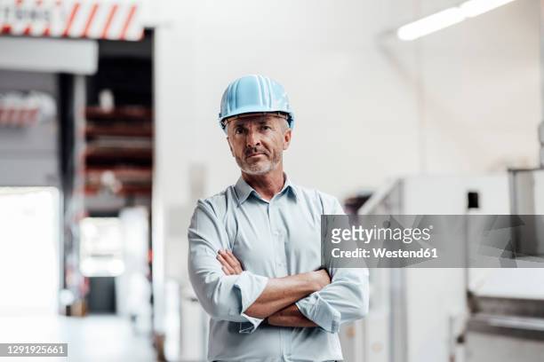 confident male engineer standing with arms crossed in industry - man with helmet stock-fotos und bilder