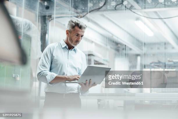 thoughtful male engineer using laptop while standing in industry - herstellendes gewerbe stock-fotos und bilder