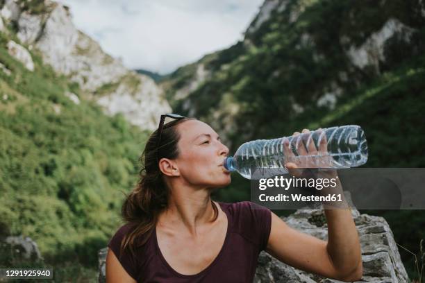 mid adult female trekker drinking from plastic water bottle while looking away - woman drinking water from bottle stock-fotos und bilder