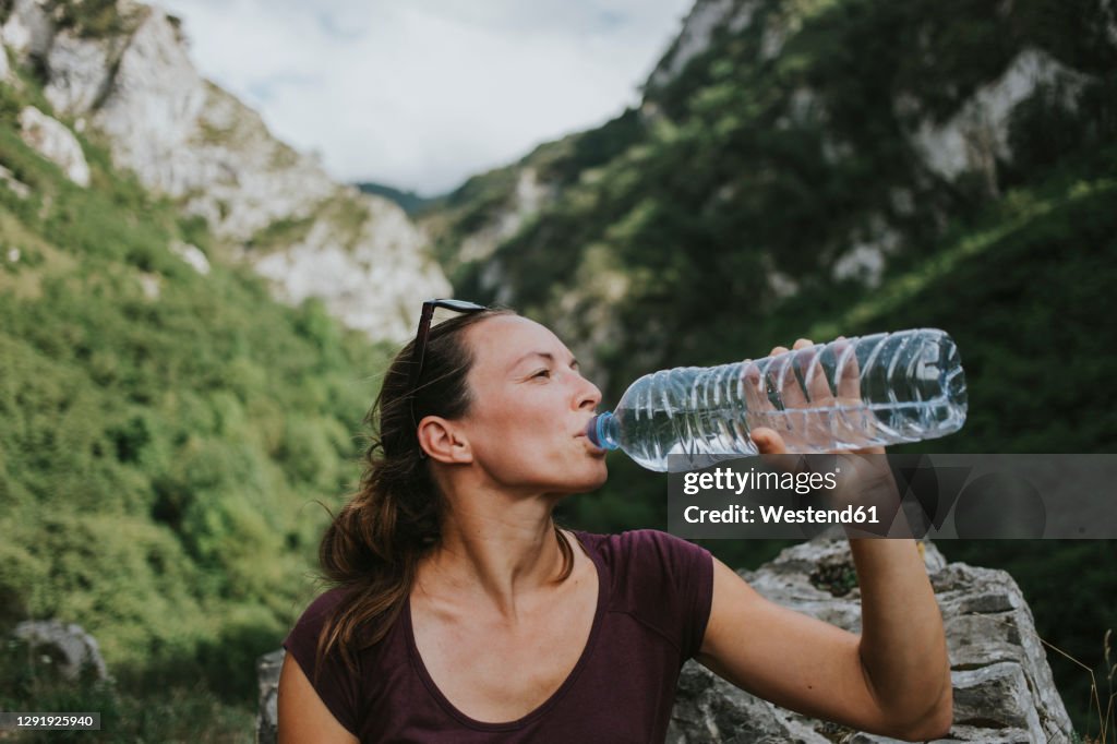 Mid adult female trekker drinking from plastic water bottle while looking away