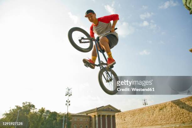 young asian man doing mid-air stunt on bmx bike against sky, hero's square, budapest, hungary - bicycle stunt stock pictures, royalty-free photos & images