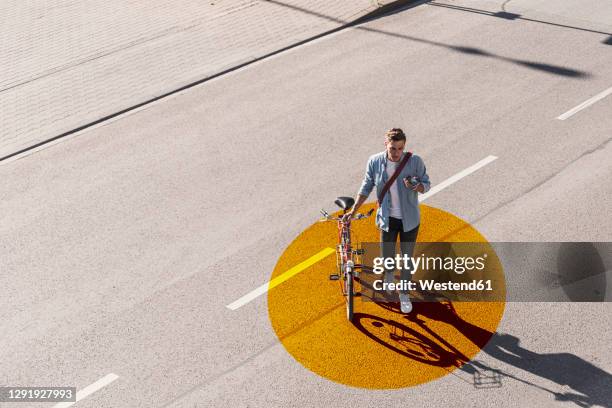 man with wheeling bicycle using mobile phone while walking on road with gold colored circle - circle of people stockfoto's en -beelden