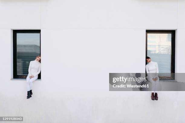 sad young women sitting on windows of white building during covid-19 - social distancing friends stock pictures, royalty-free photos & images