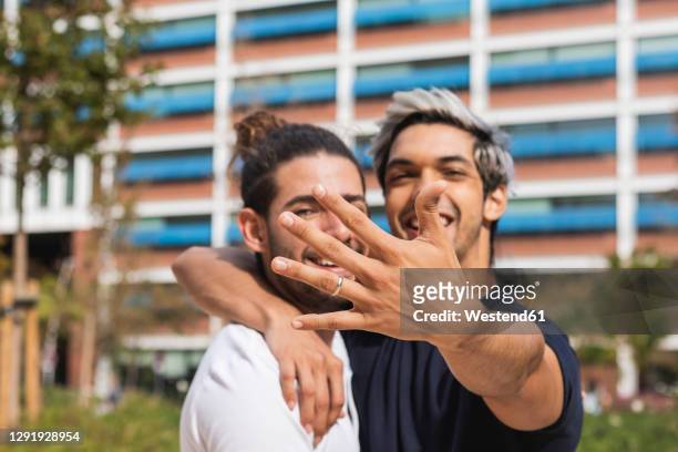 smiling man showing engagement ring while standing by gay partner in park - engagement ring stock pictures, royalty-free photos & images