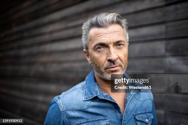 mature man staring while standing against wooden wall - handsome man imagens e fotografias de stock