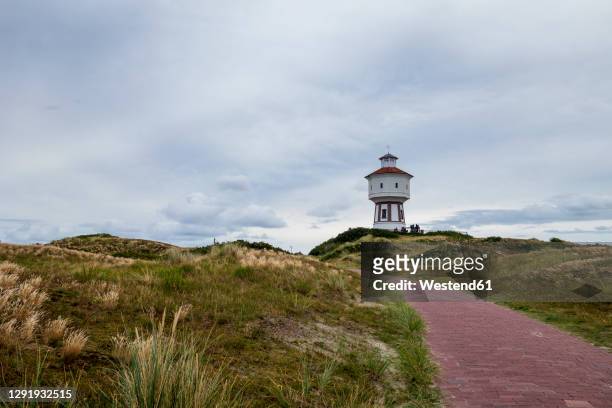 footpath stretching in front of lighthouse onlangeoog island - langeoog stock pictures, royalty-free photos & images