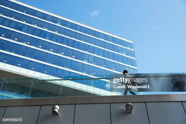 businessman with backpack walking on footbridge by office building in downtown district - bridge building glass stock pictures, royalty-free photos & images