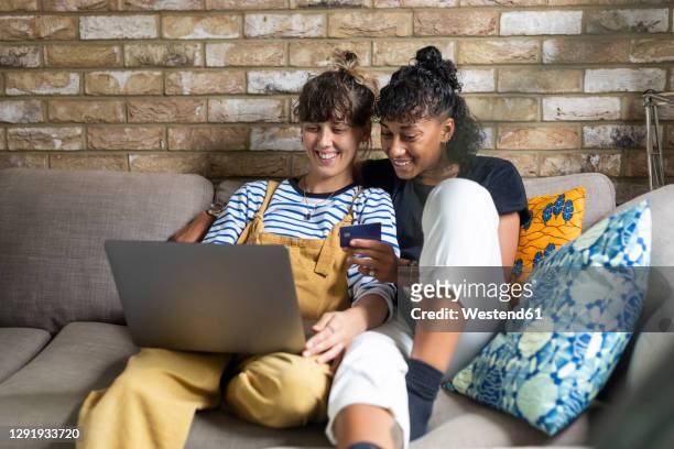 smiling lesbian couple doing online shopping while sitting at home - girlfriend stock pictures, royalty-free photos & images