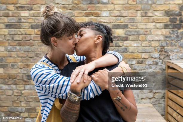 lesbian couple kissing each other while standing at back yard - gay couple kissing fotografías e imágenes de stock
