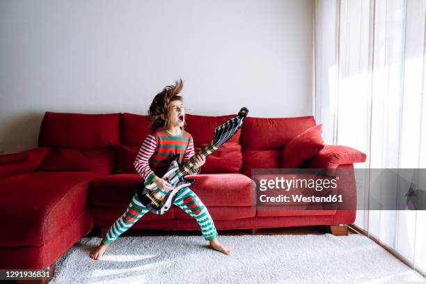 happy girl playing guitar against sofa in living room - guitar photos et images de collection