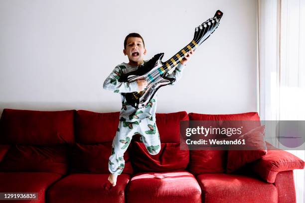 boy jumping from sofa while playing guitar in living room - boy singing stock pictures, royalty-free photos & images