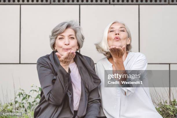 happy businesswoman blowing kiss while sitting against building - enviar un beso fotografías e imágenes de stock