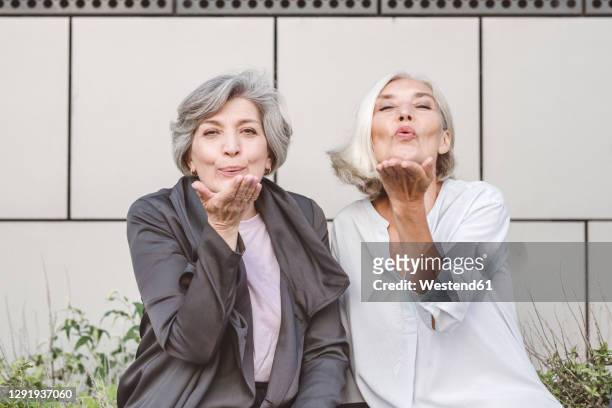 happy businesswoman blowing kiss while sitting against building - blowing a kiss stockfoto's en -beelden