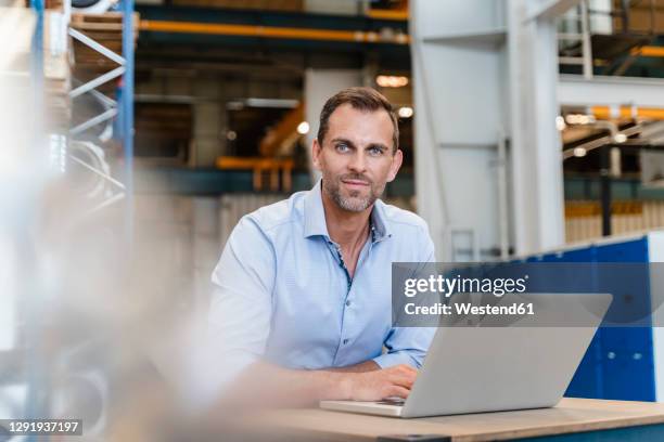 smiling businessman sitting with laptop in industry - einzelner mann über 40 stock-fotos und bilder