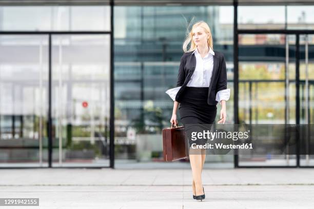 businesswoman looking away while walking with briefcase against building - businesswoman blond looking left foto e immagini stock