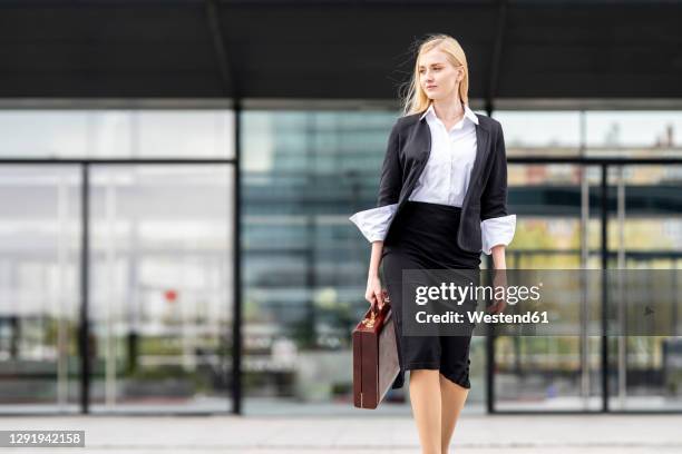 blond businesswoman walking with briefcase against building - businesswoman blond looking left foto e immagini stock