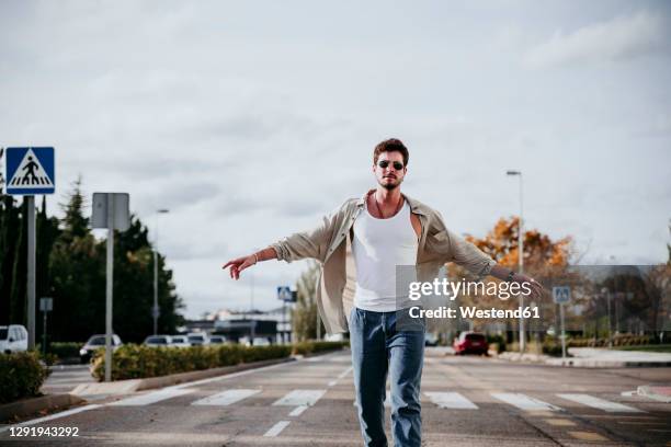 confident man with arms outstretched walking against sky during sunny day - arms outstretched fotografías e imágenes de stock