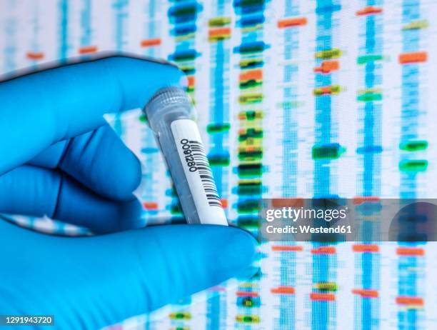scientists hand in latex glove holding vial containing sample with dna results on screen in background - bar code stock pictures, royalty-free photos & images