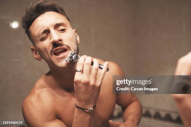 a man winks while shaving his beard with a razor blade - man shaving foam stock pictures, royalty-free photos & images
