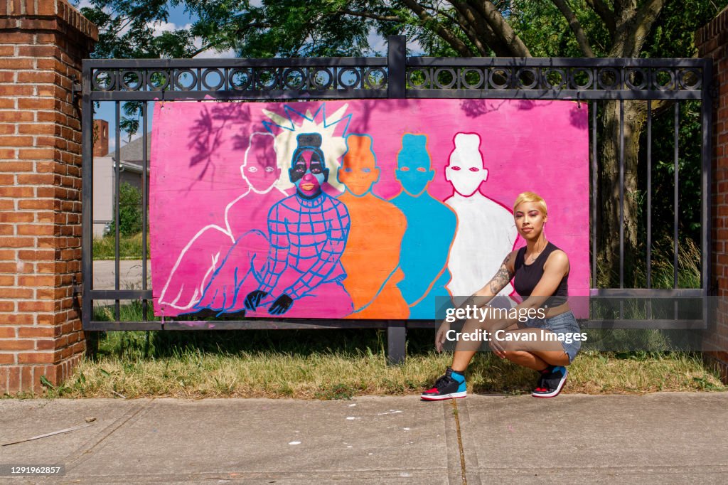 A young female artists sits proudly in front of her street painting