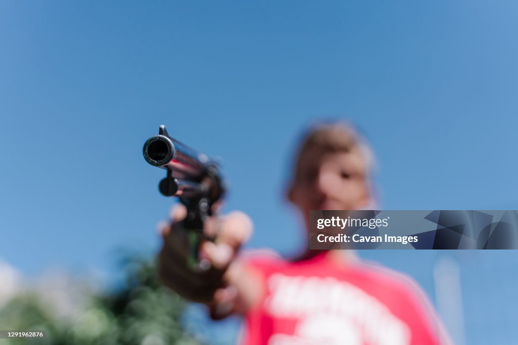 Blonde teenager wearing a red t - shirt pointing with a gun.