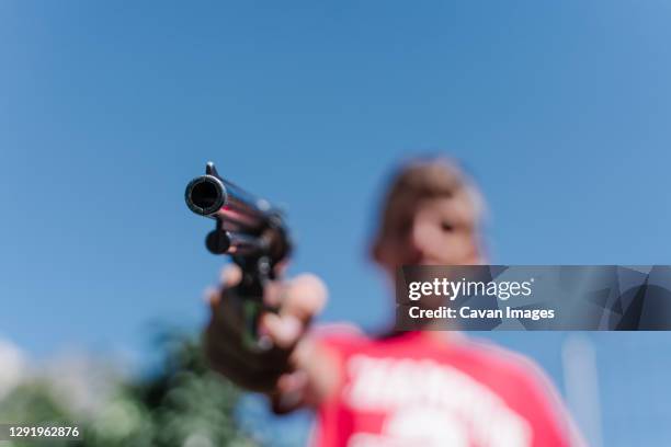 blonde teenager wearing a red t - shirt pointing with a gun. - gun stock pictures, royalty-free photos & images