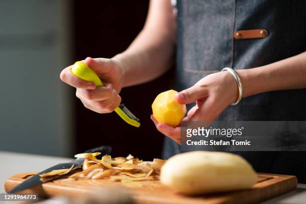 woman peeling potato in the kitchen at home - peeler stock pictures, royalty-free photos & images