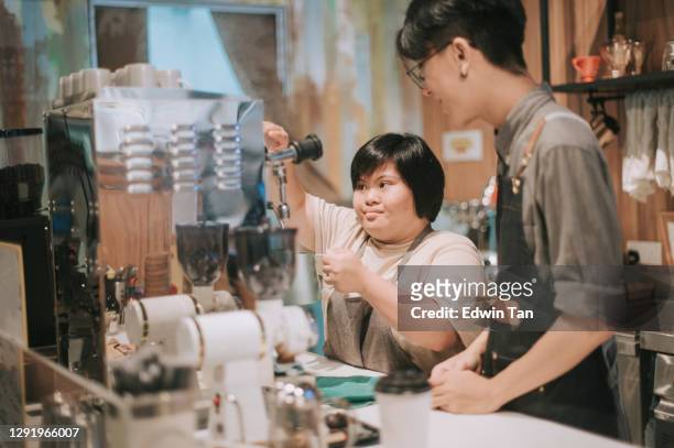 asian down syndrome female learning from barista making coffee in her café place of work - disability employment stock pictures, royalty-free photos & images