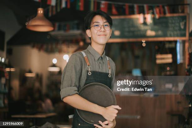 asiatische chinesische teenager junge kellner blick auf kamera lächelnde arbeit bei café-eröffnung - asian restaurant stock-fotos und bilder