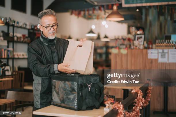 side hustle asian chinese senior man delivery picking up take away food and putting inside thermo bag at cafe - carrying food stock pictures, royalty-free photos & images