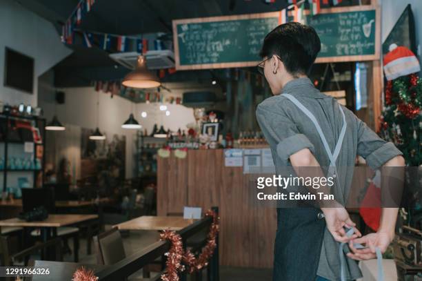 rear view asian chinese teenage boy waiter tying up apron getting read to work at cafe opening - cafe staff stock pictures, royalty-free photos & images