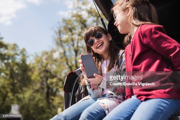 glimlachend meisje met zonnebril op het tonen van haar telefoon aan een vriend en het glimlachen - camping games stockfoto's en -beelden
