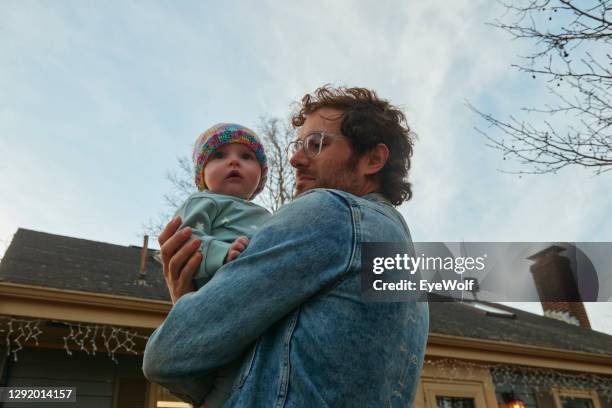 low angle shot of a young millennial father holding his young daughter close in front of their home. - framingham massachusetts stock pictures, royalty-free photos & images