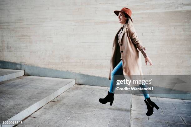 beautiful smiling woman running up on steps by wall - fashion woman jumping stock-fotos und bilder