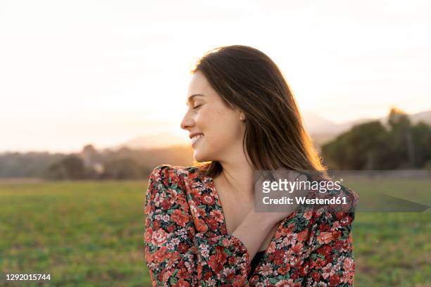 happy woman embracing herself against sky during sunset - floral pattern dress stock-fotos und bilder