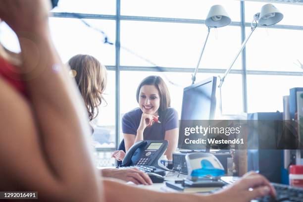 smiling businesswoman talking with female colleague while leaning on desk at office - landline phone imagens e fotografias de stock