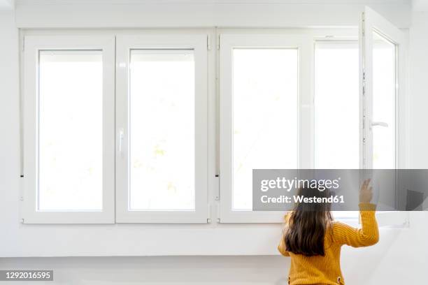 girl opening window and looking out while standing at home - open day 7 stockfoto's en -beelden