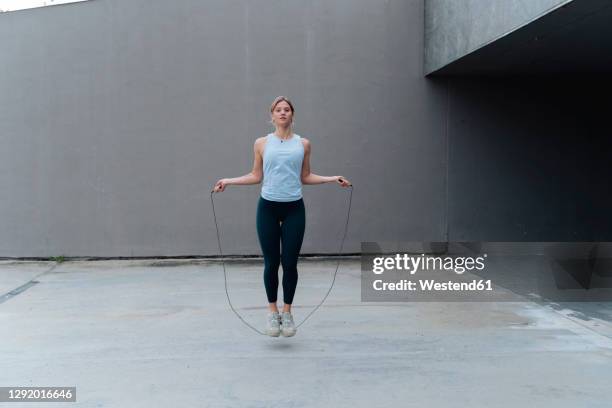 young sportswoman skipping rope while standing against wall - jump rope stock pictures, royalty-free photos & images