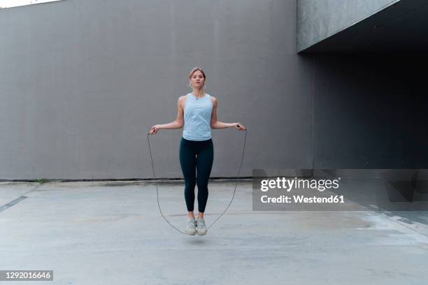 young sportswoman skipping rope while standing against wall - skipping along - fotografias e filmes do acervo