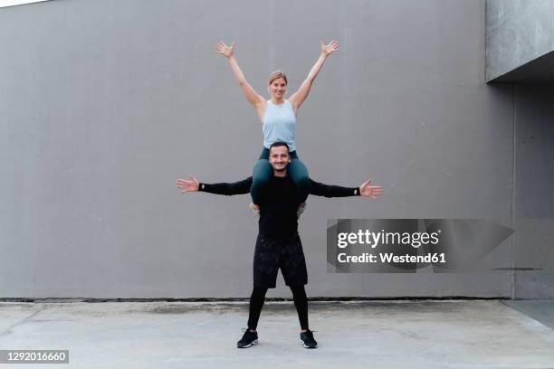 woman with hand raised sitting on man shoulder standing with arms outstretched against wall - bära på axlarna bildbanksfoton och bilder