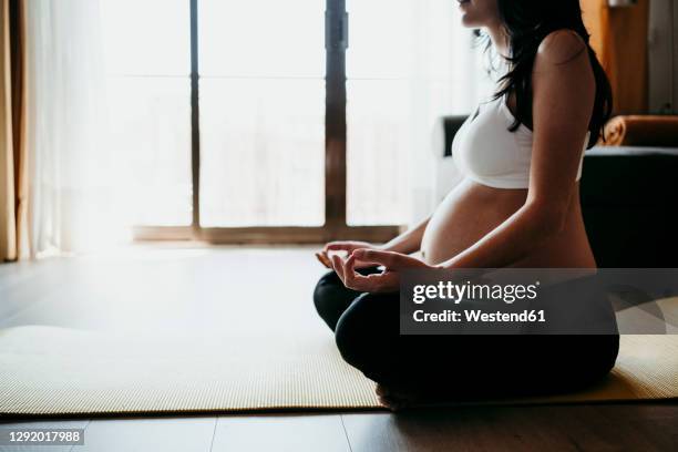 pregnant woman meditating while sitting on exercise mat at home - prenatal yoga stock pictures, royalty-free photos & images