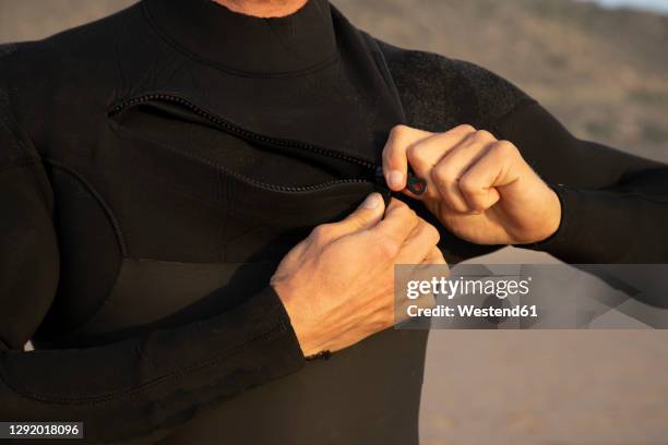 man zipping black wetsuit at beach - wetsuit stock pictures, royalty-free photos & images